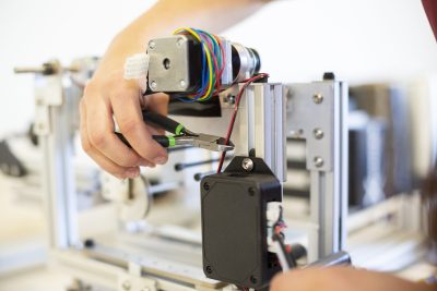 A workers right hand holding wire cutters, about to cut a wire on a device.
